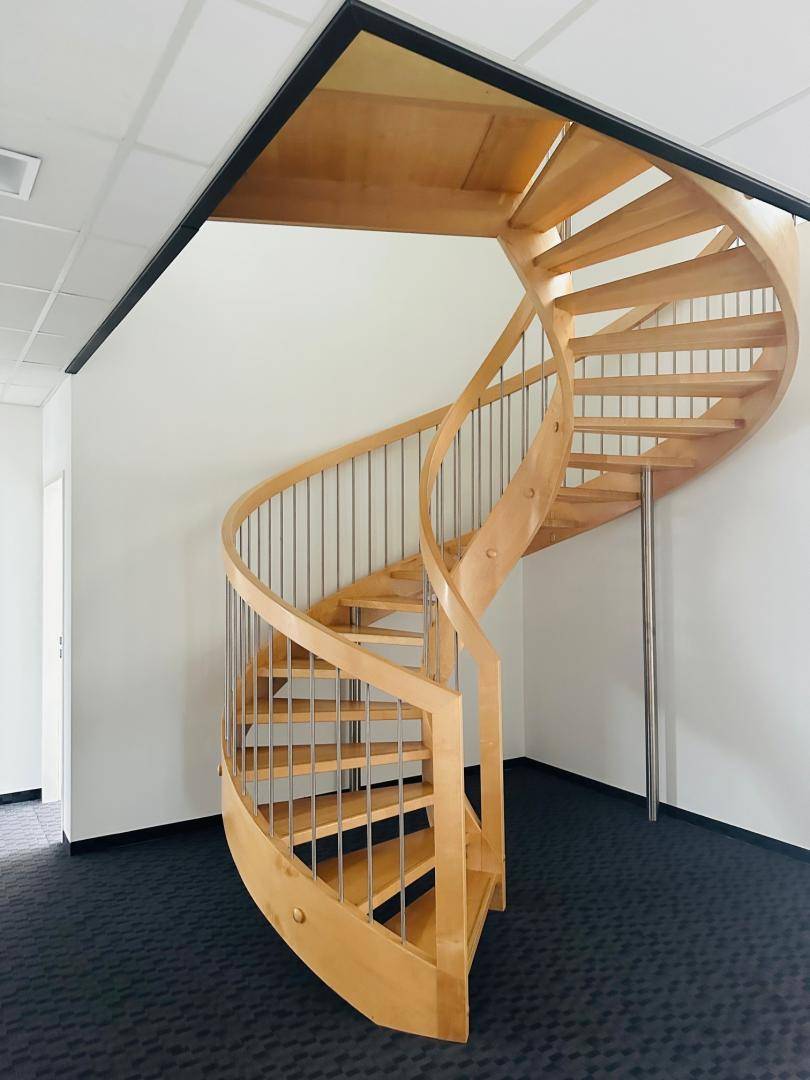 Elegante Holzwendeltreppe mit Metallgeländer in einem modernen Innenraum.