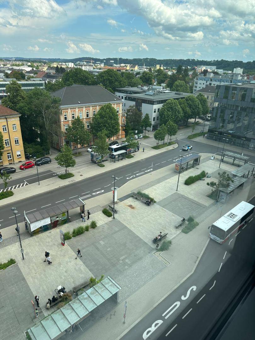Blick von oben auf eine belebte Straße mit Bushaltestellen und umliegenden Gebäuden.
