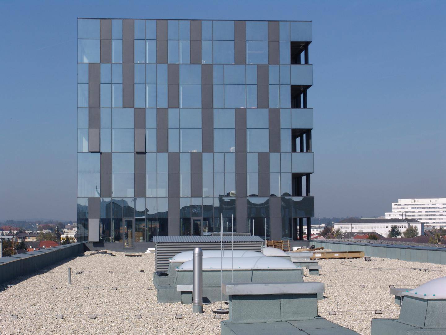 Modernes Bürogebäude mit Glasfassade und Flachdach, umgeben von Stadtlandschaft.