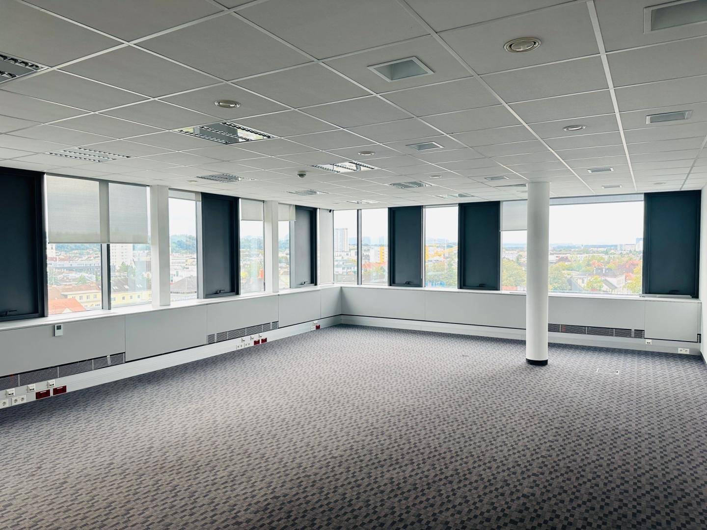 Geräumiges Büro mit Teppichboden, vielen Fenstern und abgehängter Decke.