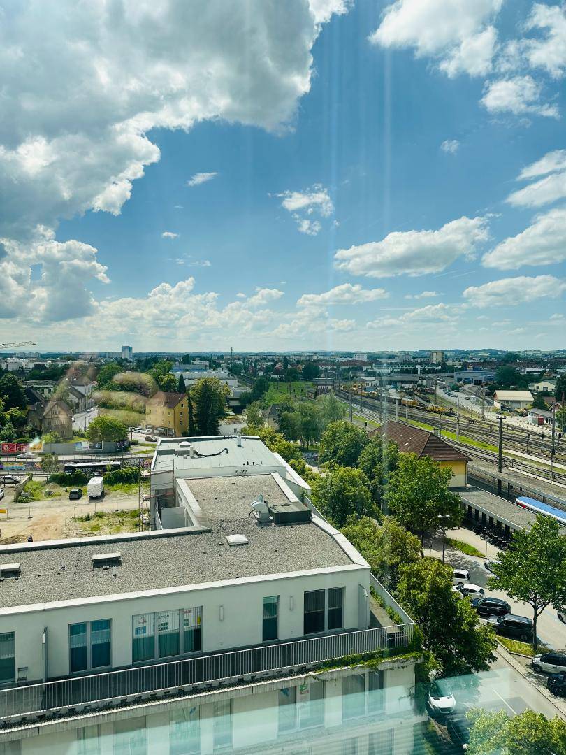 Weitläufiger Stadtblick mit Bahngleisen und Gebäuden unter blauem Himmel mit Wolken.