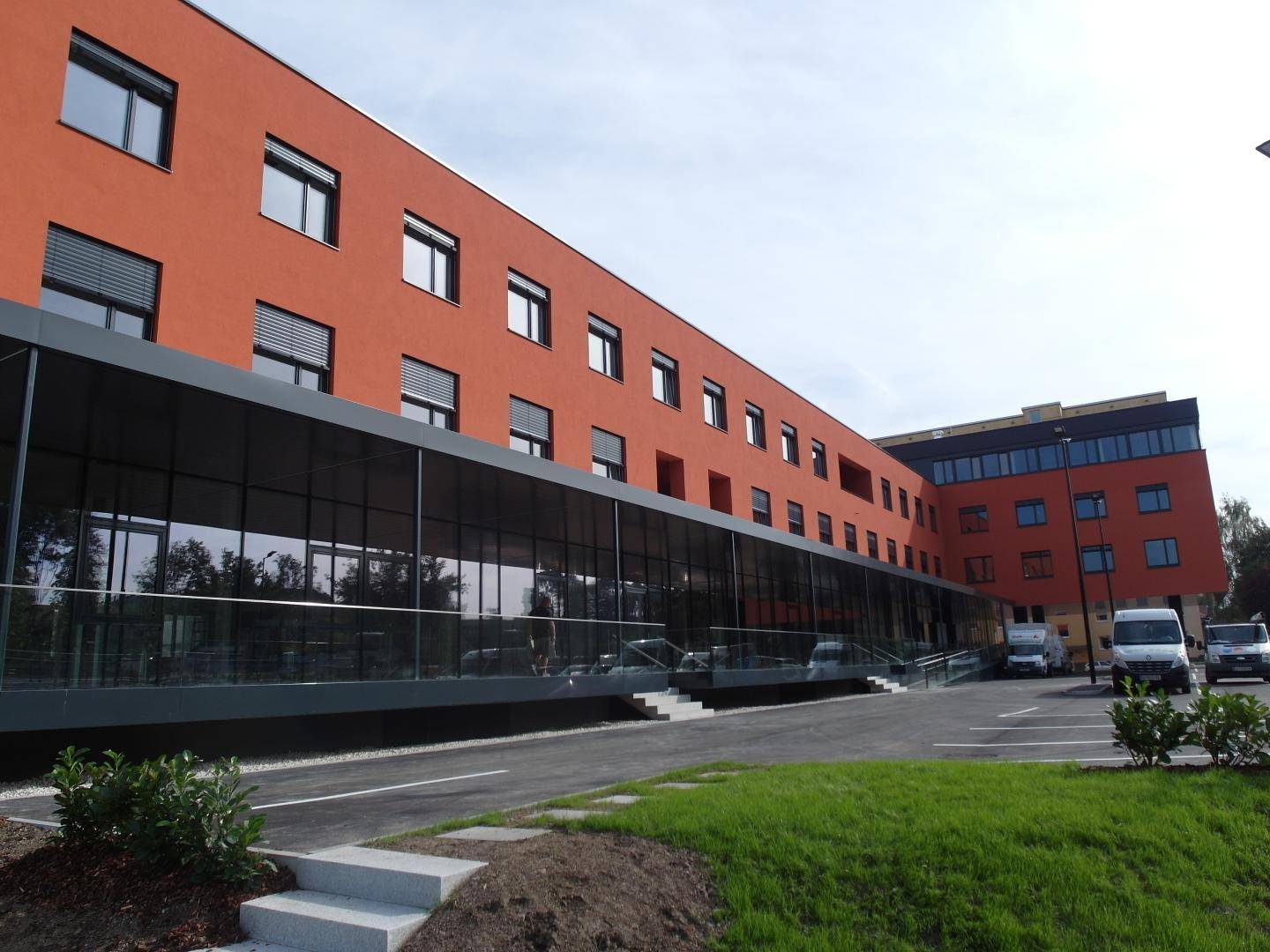 Modernes Geschäftsgebäude mit orangefarbener Fassade, Glasfront und gepflegter Grünfläche.