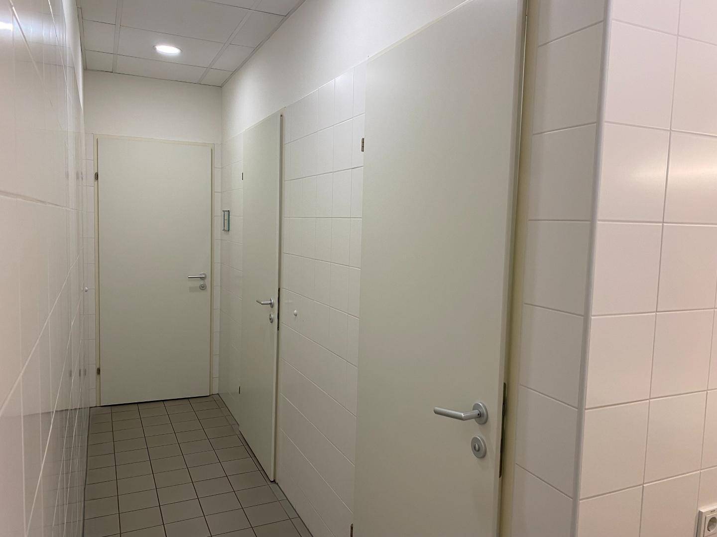 Heller Flur mit weißen Fliesenwänden und mehreren Türen zu Sanitärräumen.