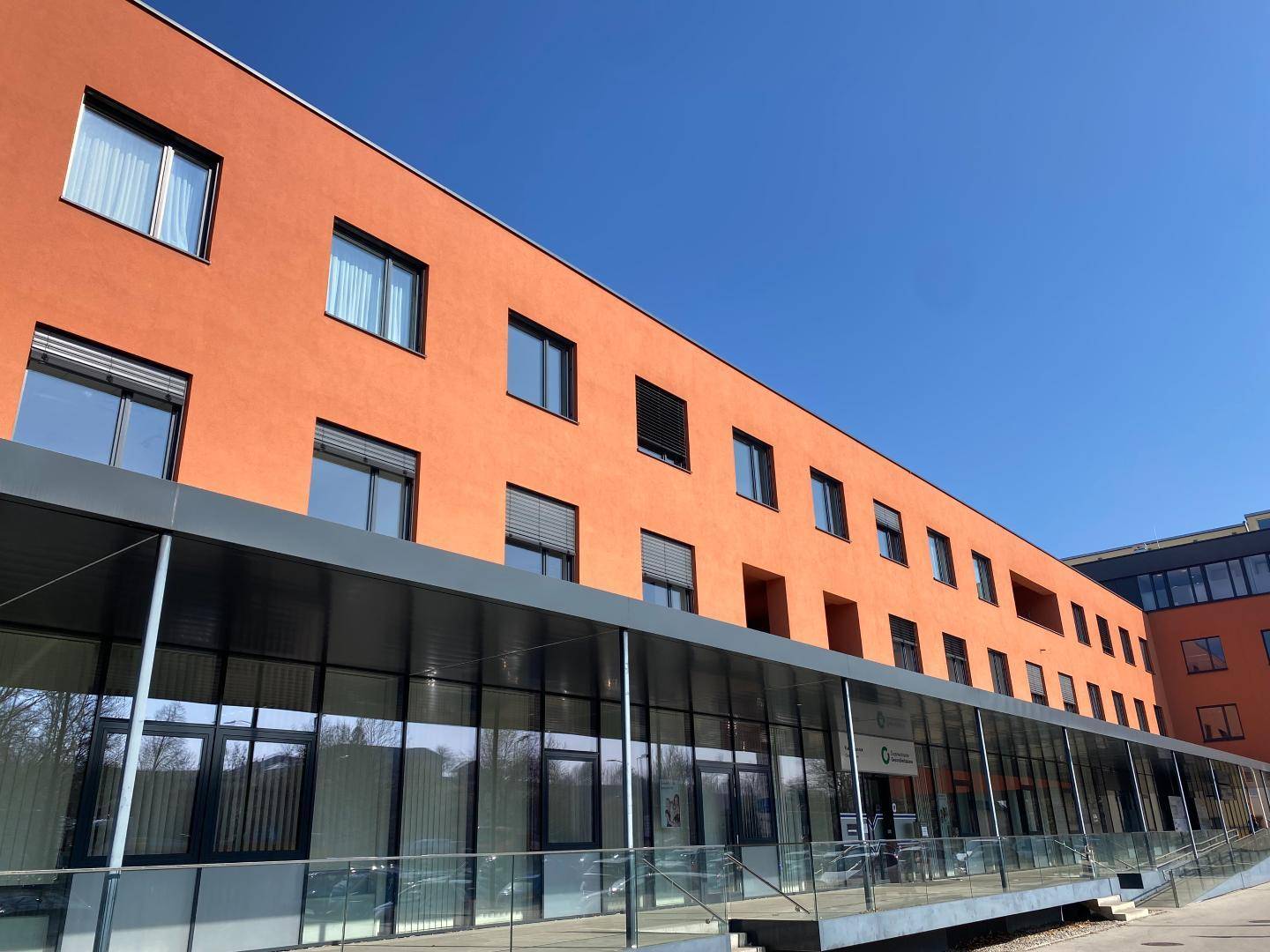 Lange Ansicht eines modernen Geschäftsgebäudes mit orangefarbener Fassade und durchgehender Glasfront.