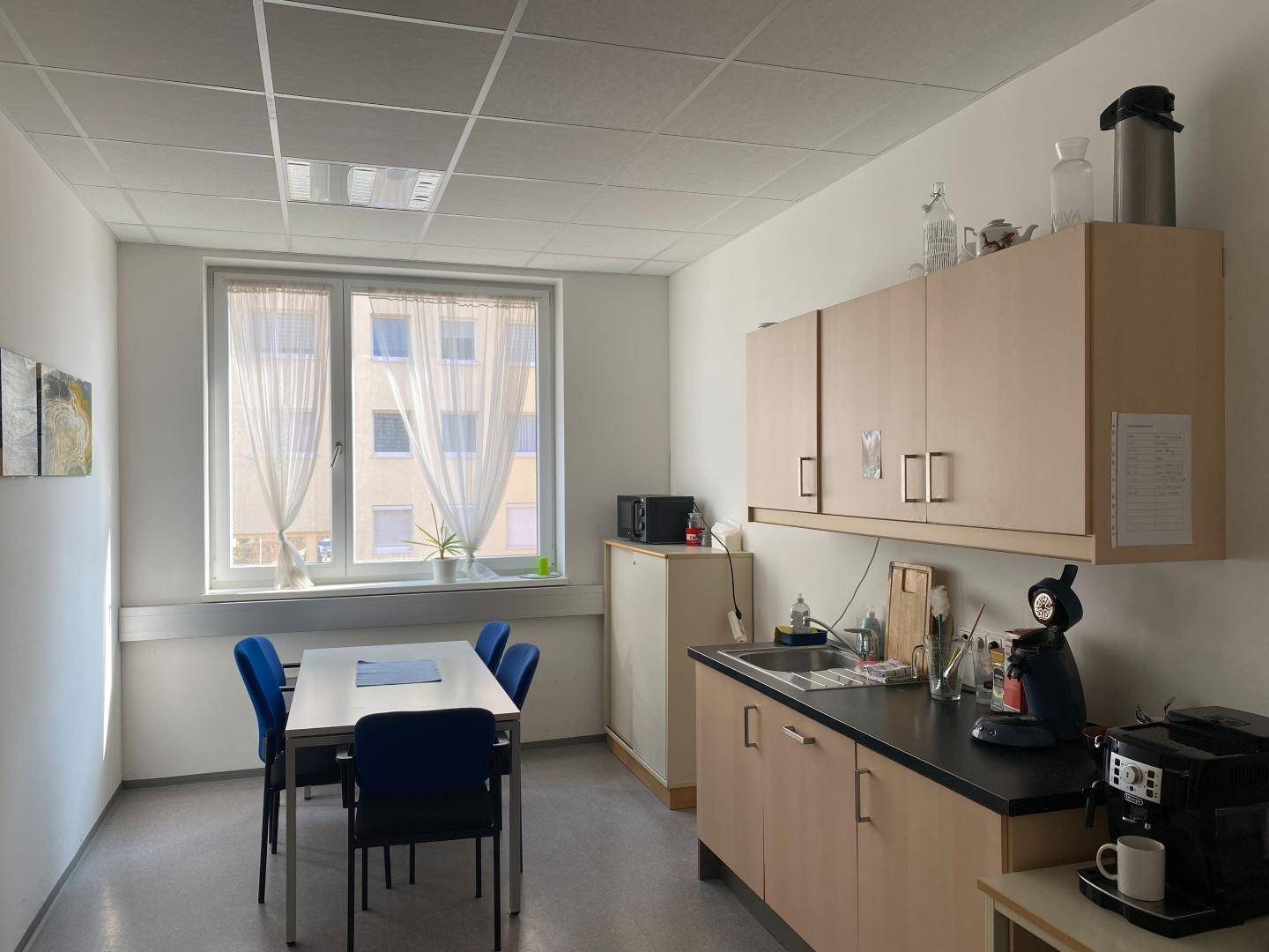 Funktionale Büroküche mit hellen Holzschränken, Spüle und Kaffeemaschine.