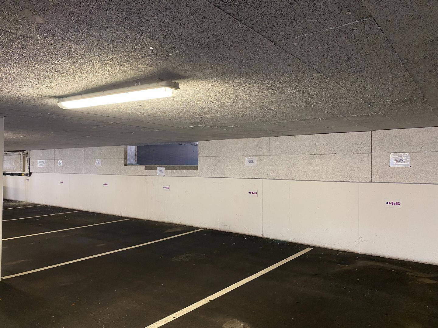 Leere Tiefgarage mit Betonwänden und Deckenbeleuchtung, bereit für Fahrzeuge.