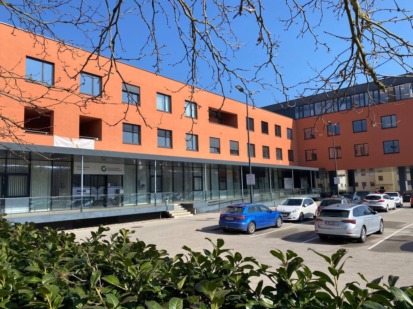 Modernes Geschäftsgebäude mit orangefarbener Fassade und Parkplätzen unter blauem Himmel.