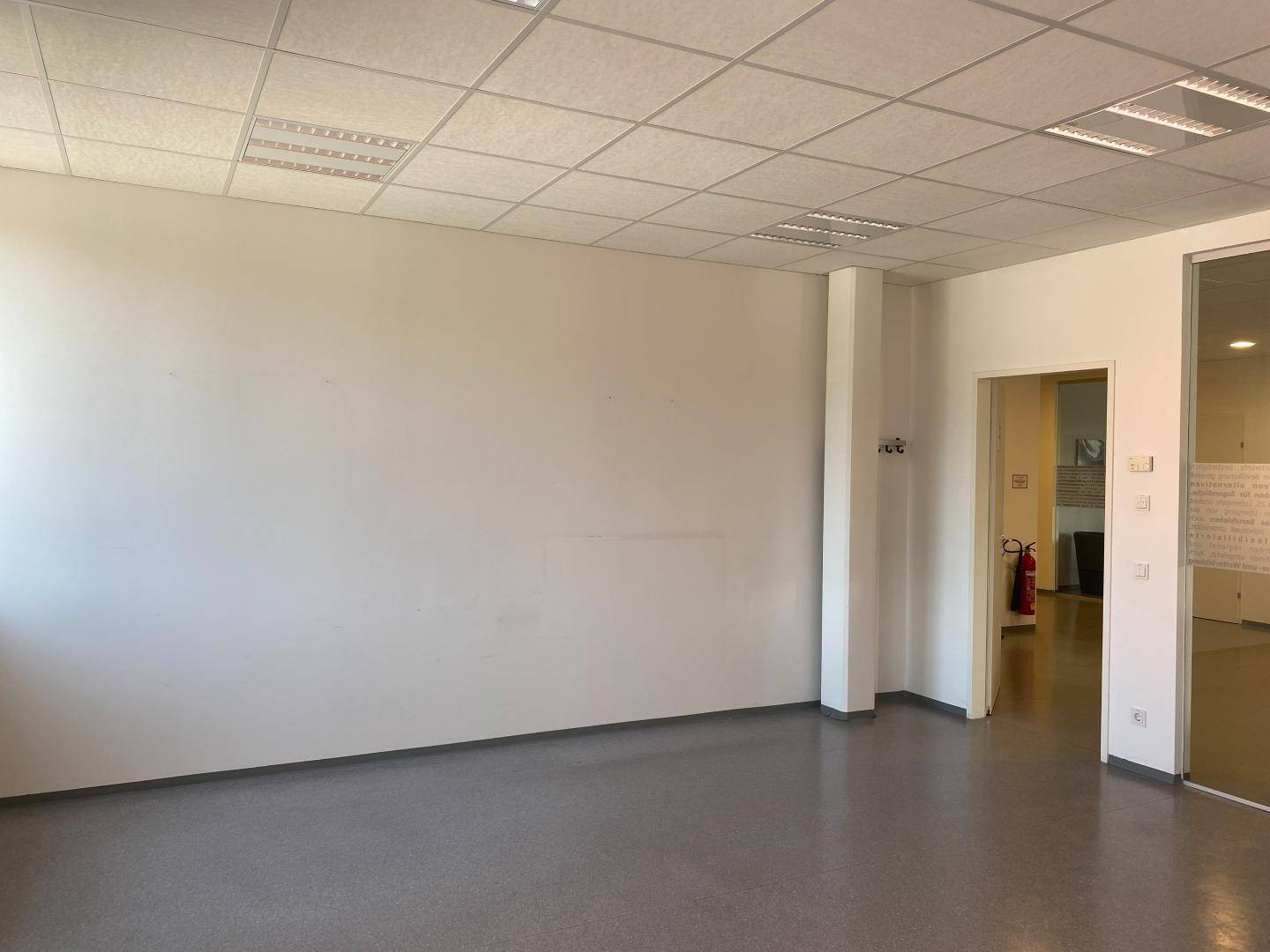 Leerer, heller Büroraum mit grauen Bodenfliesen und weiß gestrichenen Wänden.