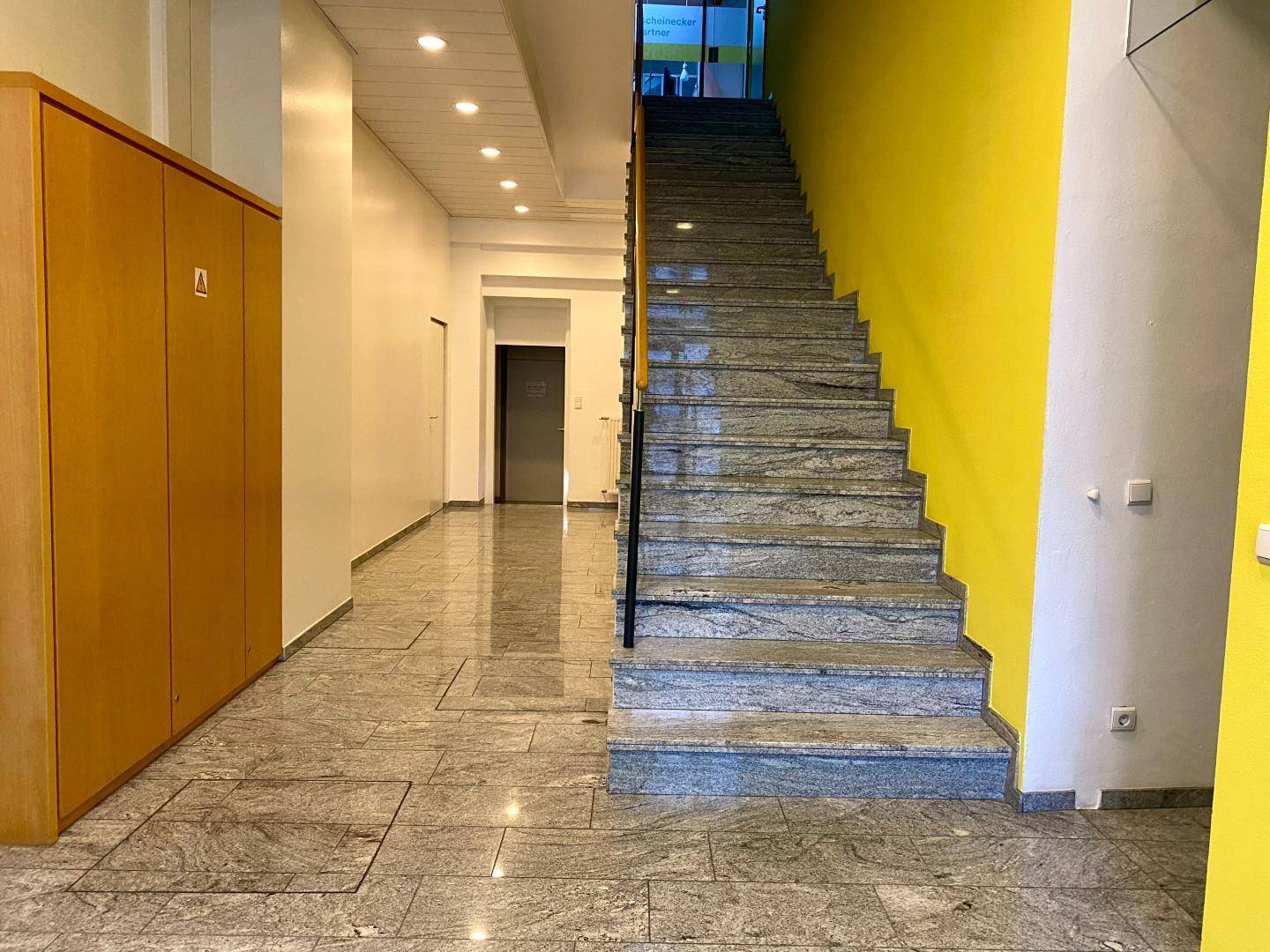 Eingangsbereich mit Steinfliesenboden, Treppe und Holzschränken.