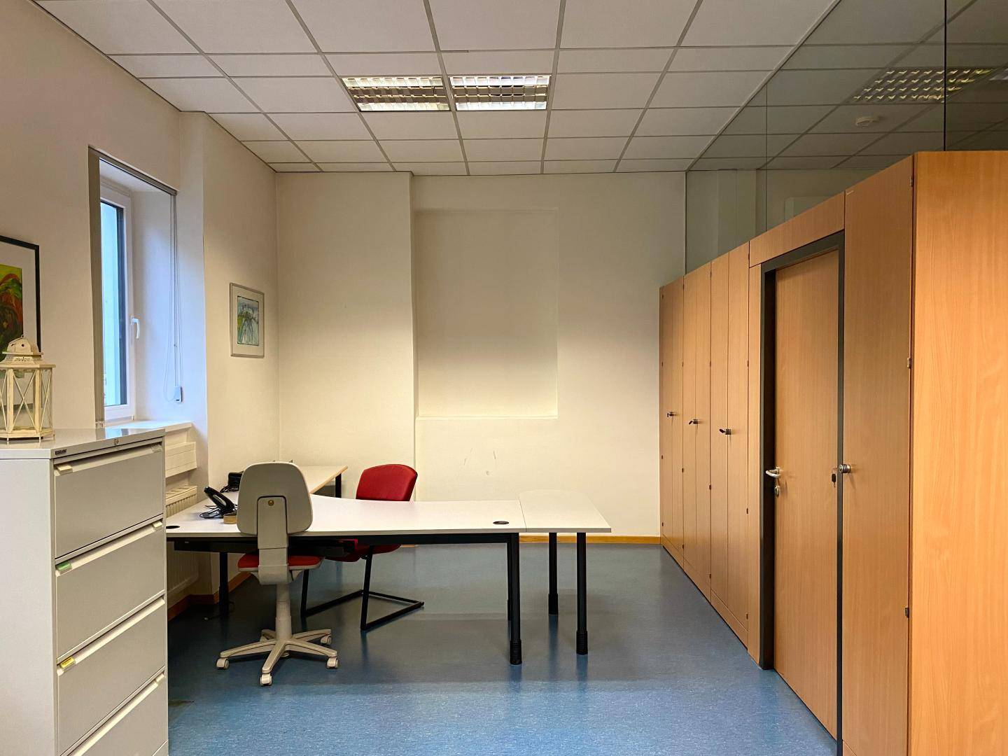Büroraum mit Schreibtischen, Aktenschrank und integrierten Holzschränken.