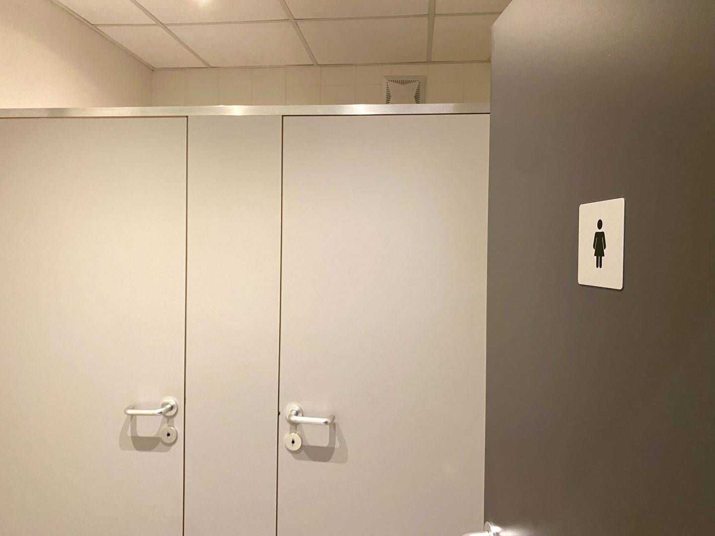 Toilettenkabinen in einem öffentlichen Waschraum mit weißer Trennwand.