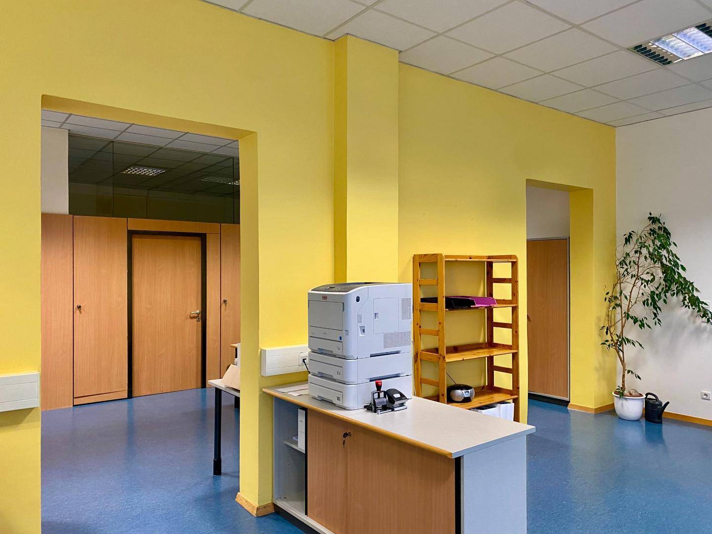 Bürobereich mit gelben Wänden, Holztüren und einem Drucker auf einem Schrank.