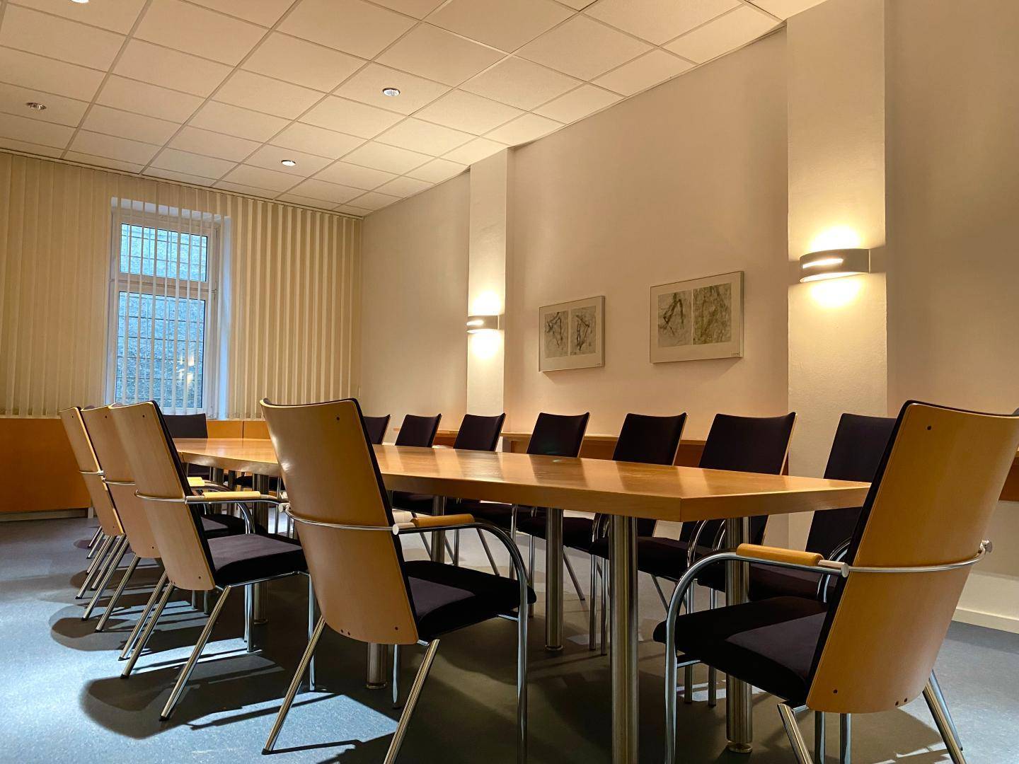 Großer Konferenzraum mit langem Holztisch, vielen Stühlen und Fenstern.