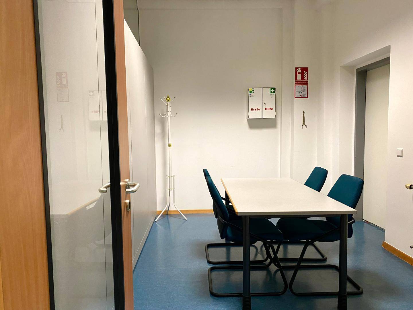 Besprechungsraum mit Tisch, Stühlen, Erste-Hilfe-Kasten und Feuerlöscher.
