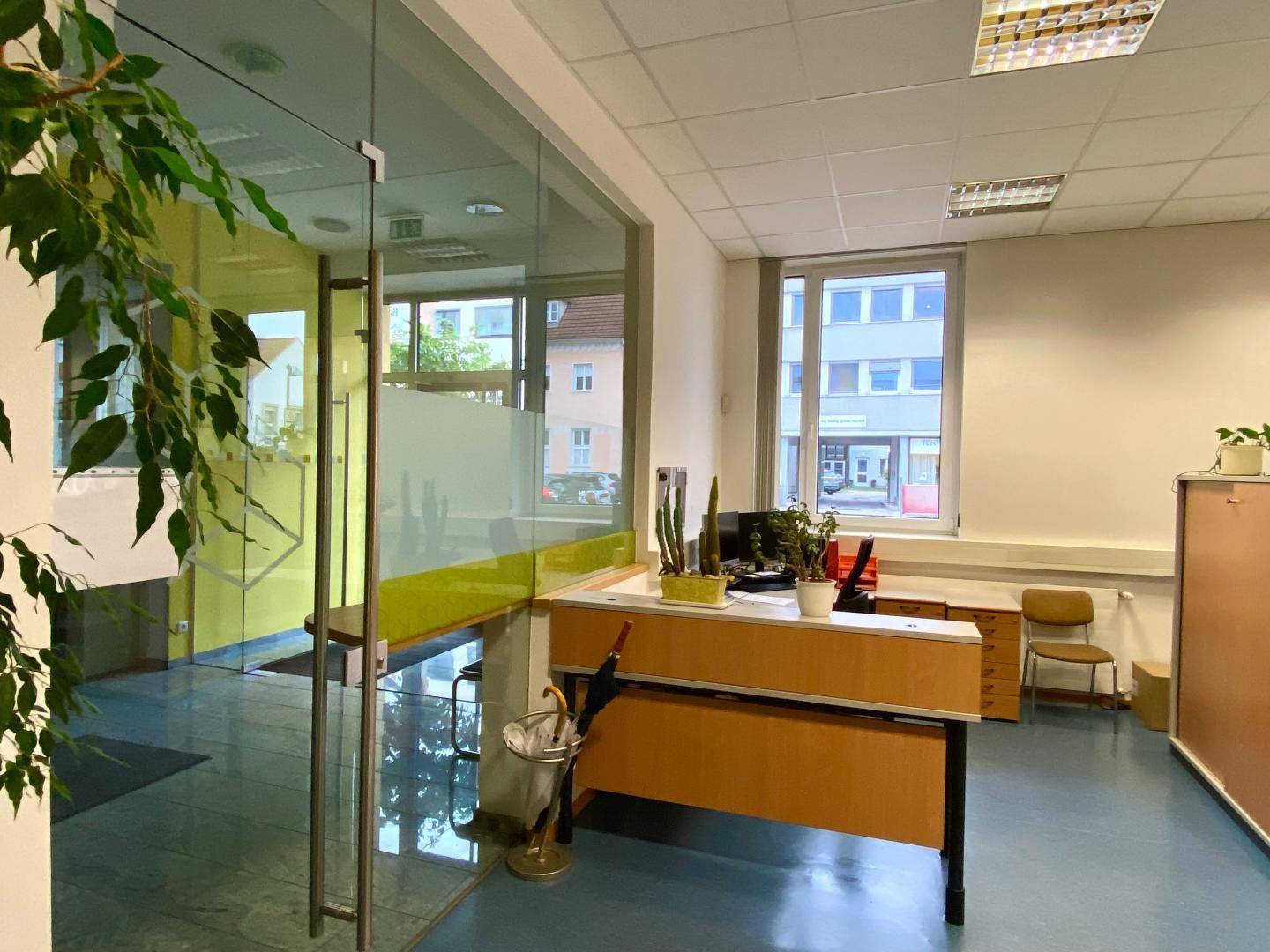 Helles Büro mit Glastrennwand, Schreibtischen und Blick auf die Straße.