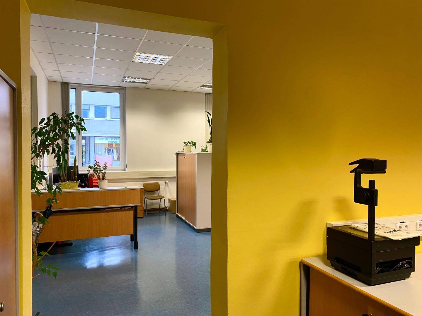 Blick durch einen Türrahmen in einen hellen Bürobereich mit Schreibtischen.