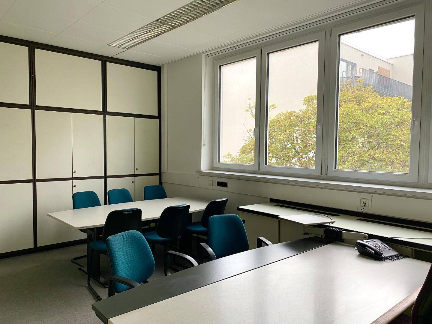 Konferenzraum mit einem langen Tisch, Stühlen und integrierten Schränken, mit Blick ins Grüne.
