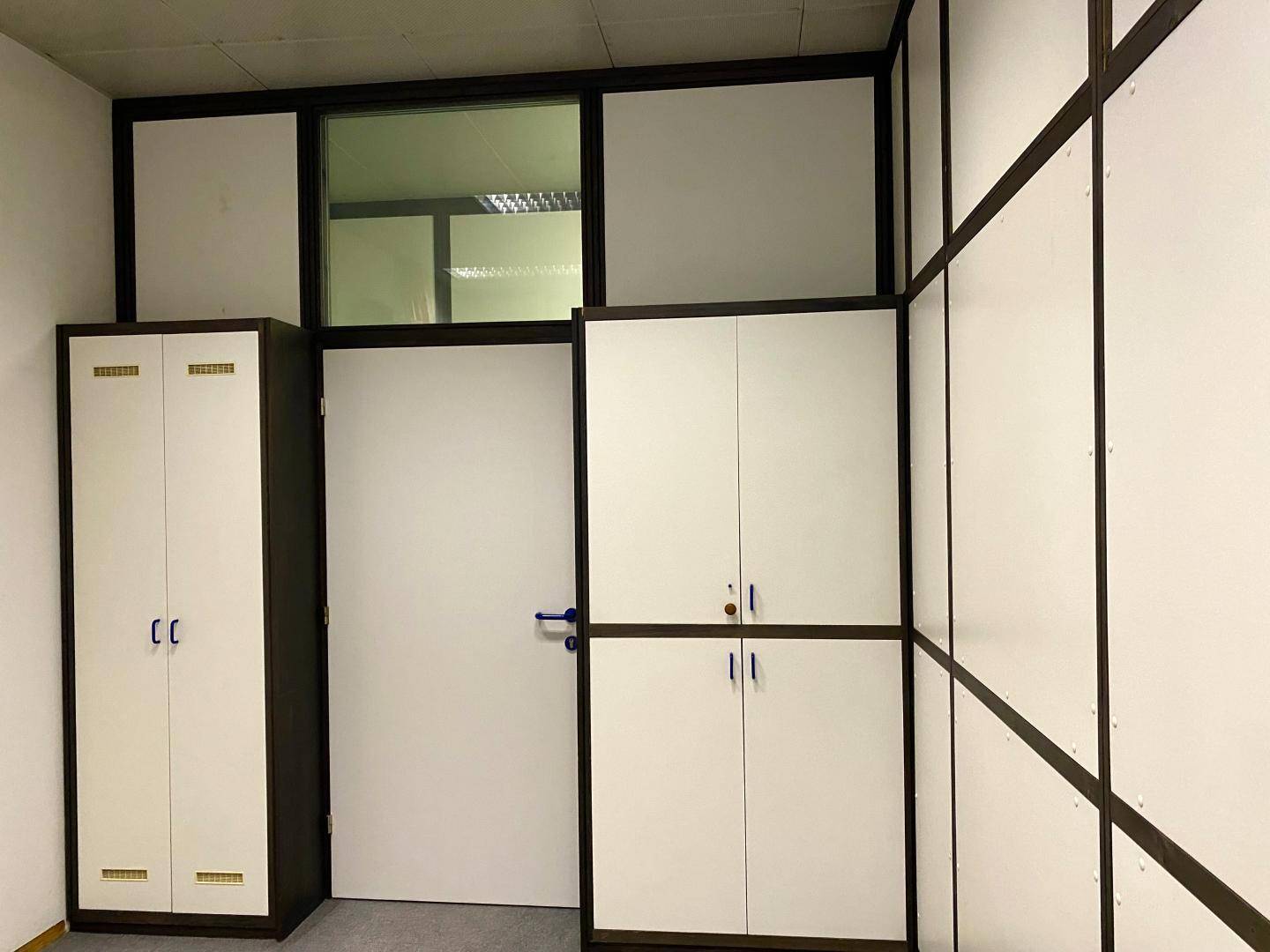 Büro mit integrierten Schränken und einer Tür mit Glasoberlicht, die zu einem weiteren Raum führt.