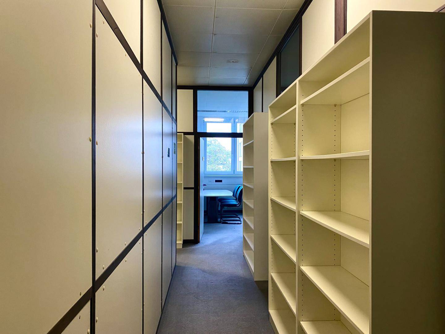 Langer Flur mit integrierten Schränken und Regalen, der zu einem Büro führt.