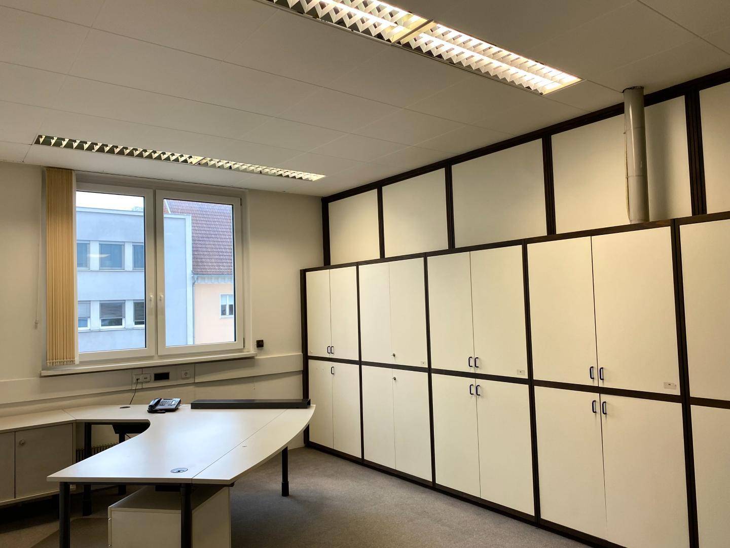 Büro mit einem großen Schreibtisch, integrierten Schränken und einem Fenster mit Jalousien.
