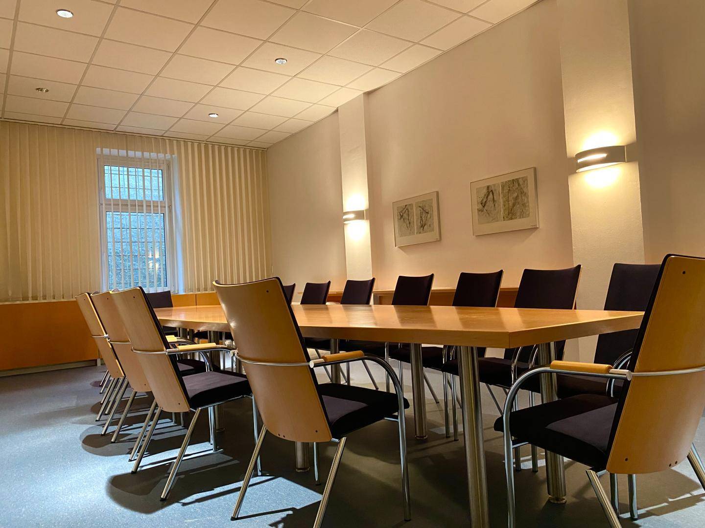 Großer Konferenzraum mit einem langen Holztisch, vielen Stühlen und indirekter Beleuchtung.