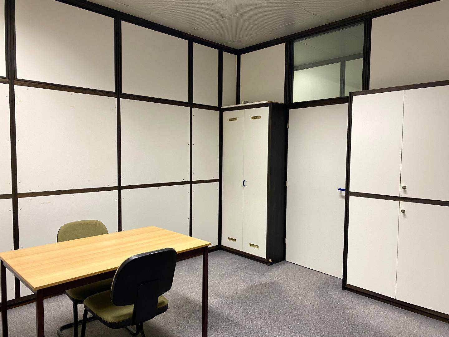 Büro mit modularen Trennwänden, integrierten Schränken und einem Holztisch für Besprechungen.