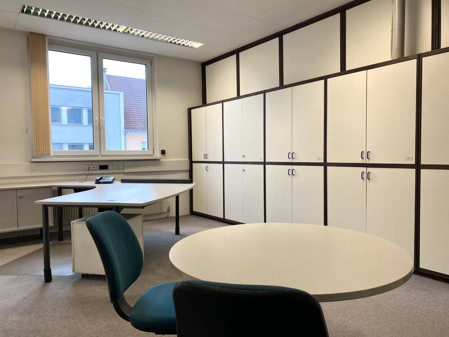 Büro mit einem Schreibtisch, einem runden Besprechungstisch und vielen integrierten Schränken.