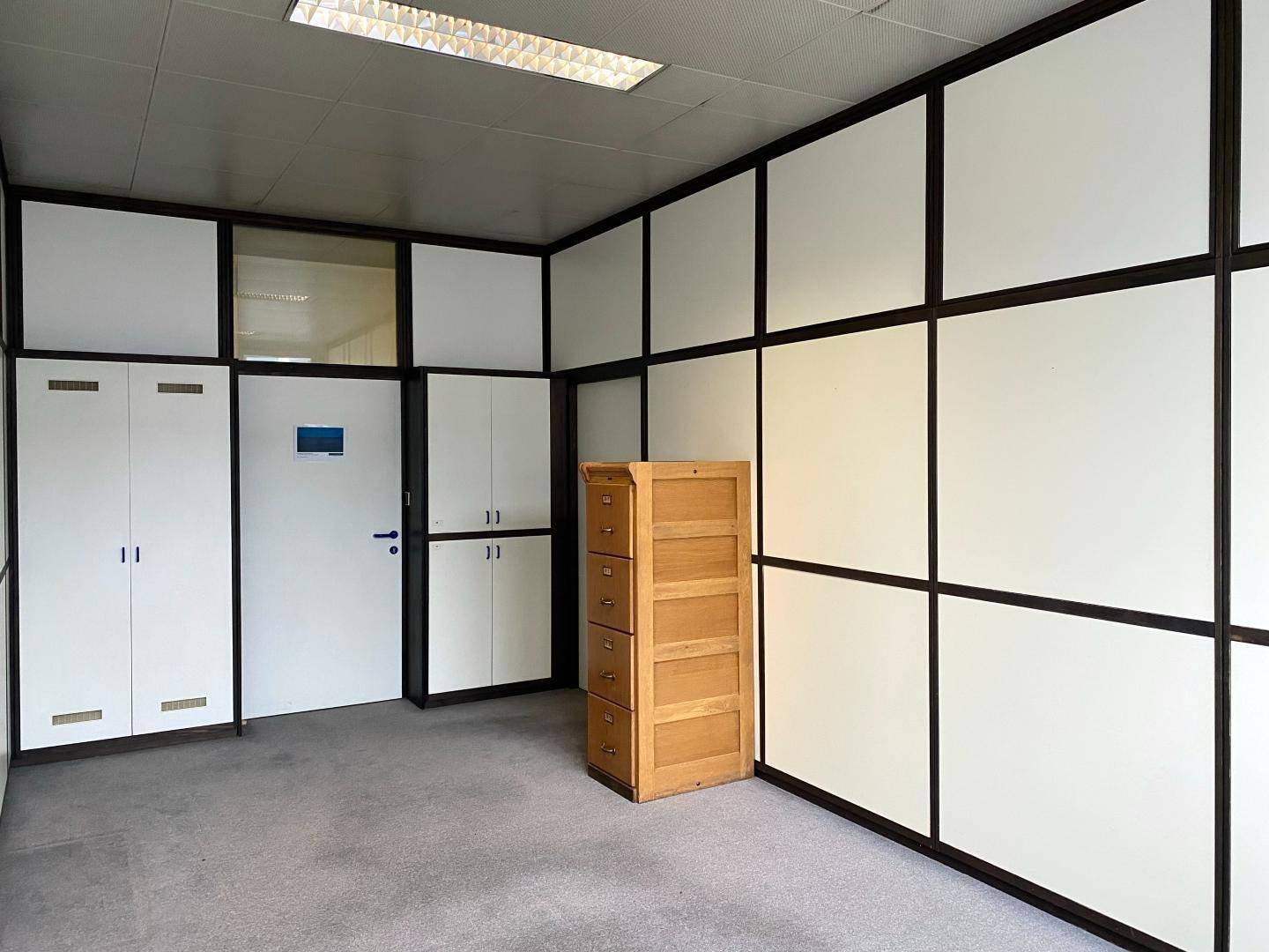 Büro mit modularen Trennwänden, integrierten Schränken und einem Holzaktenschrank.