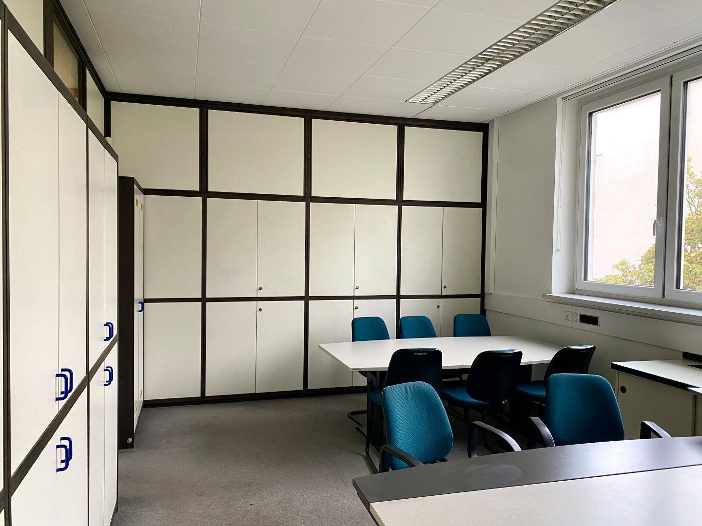 Konferenzraum mit einem langen Tisch, Stühlen und integrierten Schränken entlang der Wand.