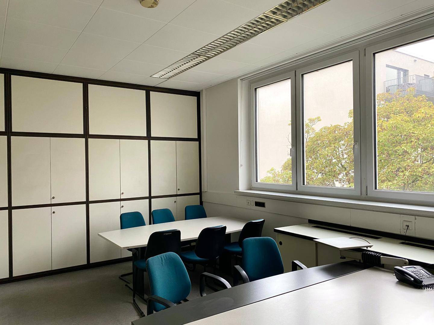 Konferenzraum mit einem langen Tisch, Stühlen und integrierten Schränken, mit Blick ins Grüne.