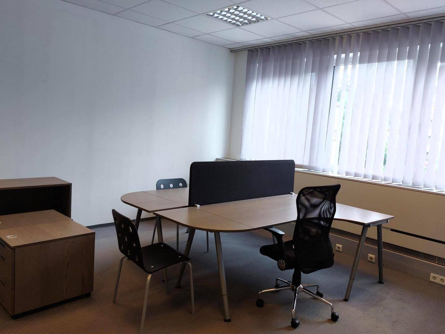 Detailansicht eines Büroraums mit ergonomischen Bürostühlen und Schreibtischen vor einem großen Fenster.