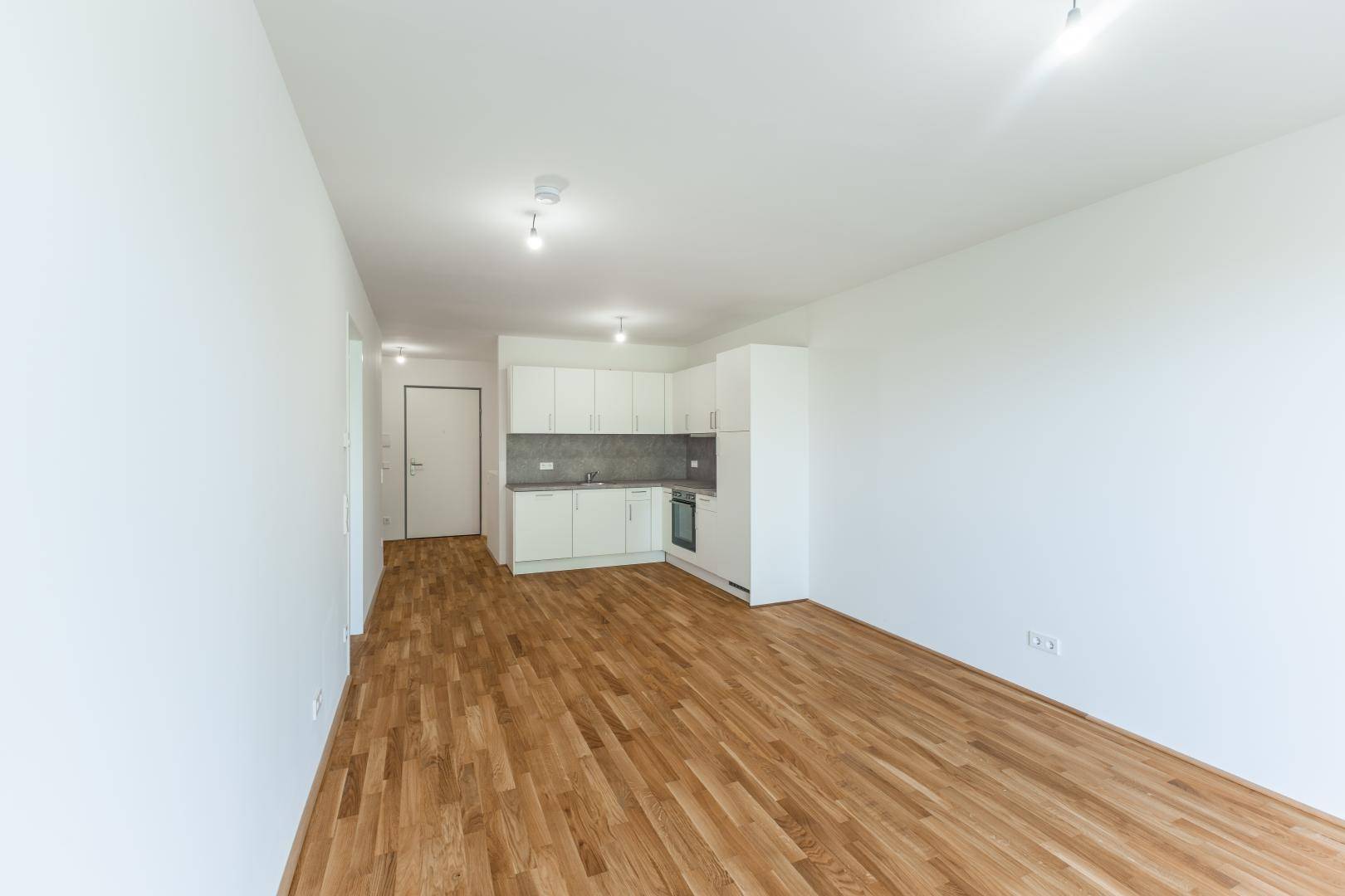 Geräumiger Wohnbereich mit integrierter Küchenzeile und hellem Holzboden in Neubauwohnung.