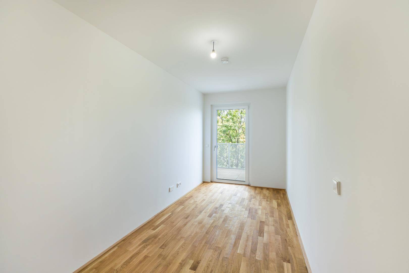 Helles Schlafzimmer mit Holzboden und Zugang zu einem kleinen Balkon oder einer französischen Brüstung.