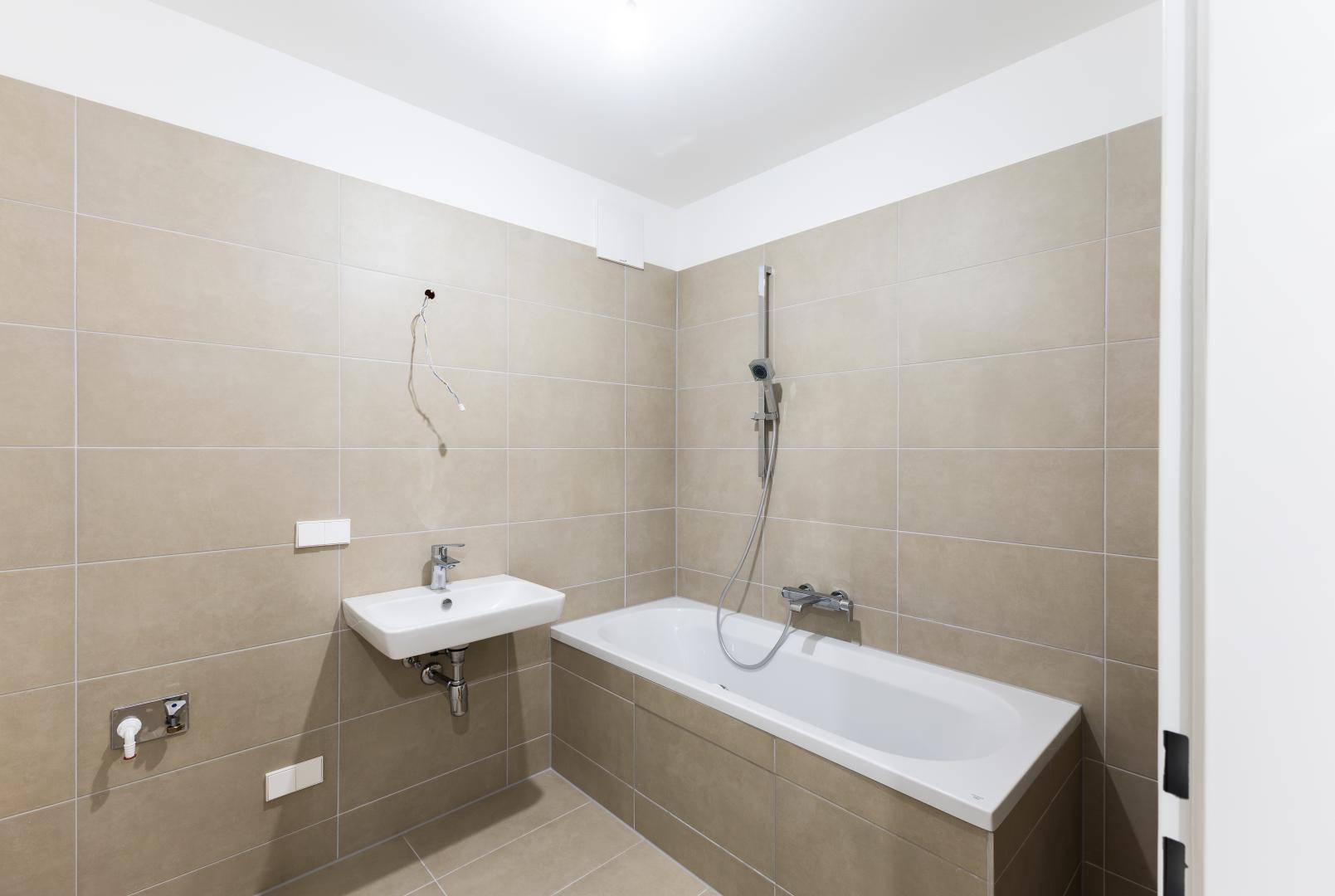 Modernes Badezimmer mit beigefarbenen Fliesen, Badewanne und einem einzelnen Waschbecken.