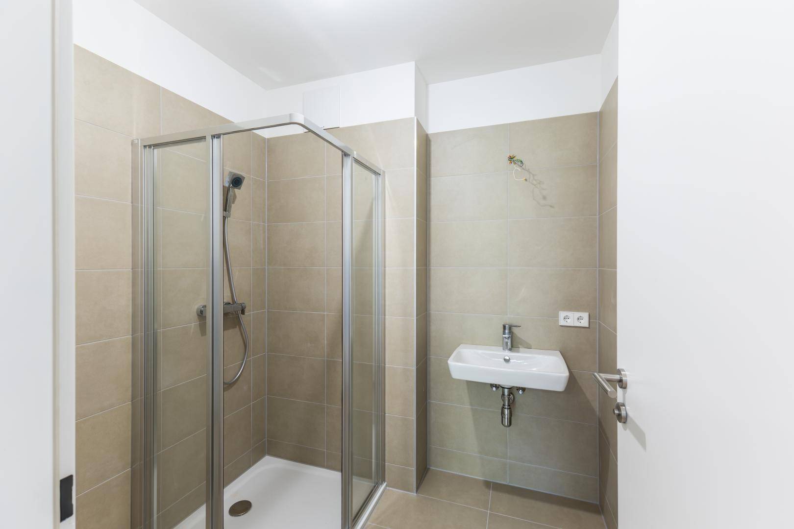 Modernes Badezimmer mit beigefarbenen Fliesen, Duschkabine und einem einzelnen Waschbecken.