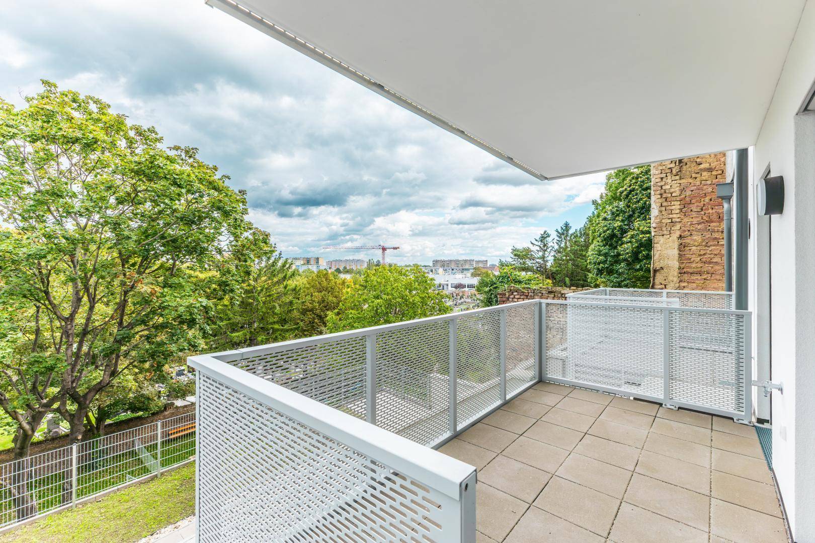 Geräumiger Balkon mit Fliesenboden und Blick ins Grüne sowie auf die Stadt.