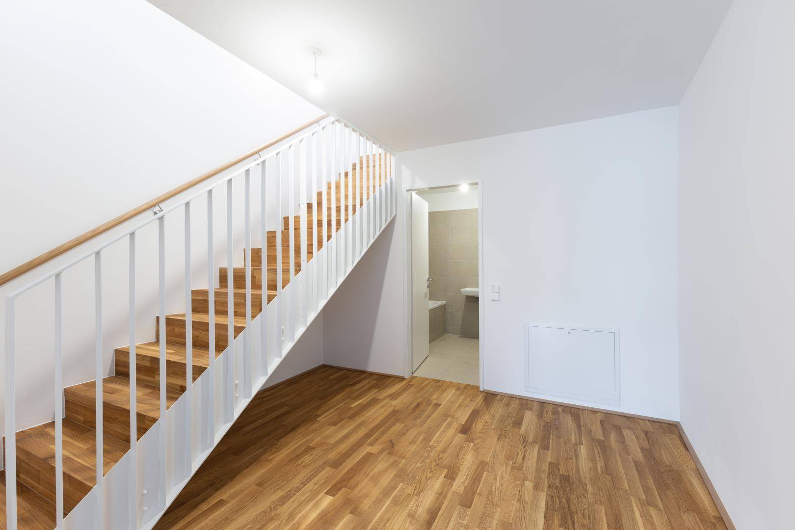 Heller Flur mit Holztreppe und Parkettboden, der zu einem Badezimmer führt.