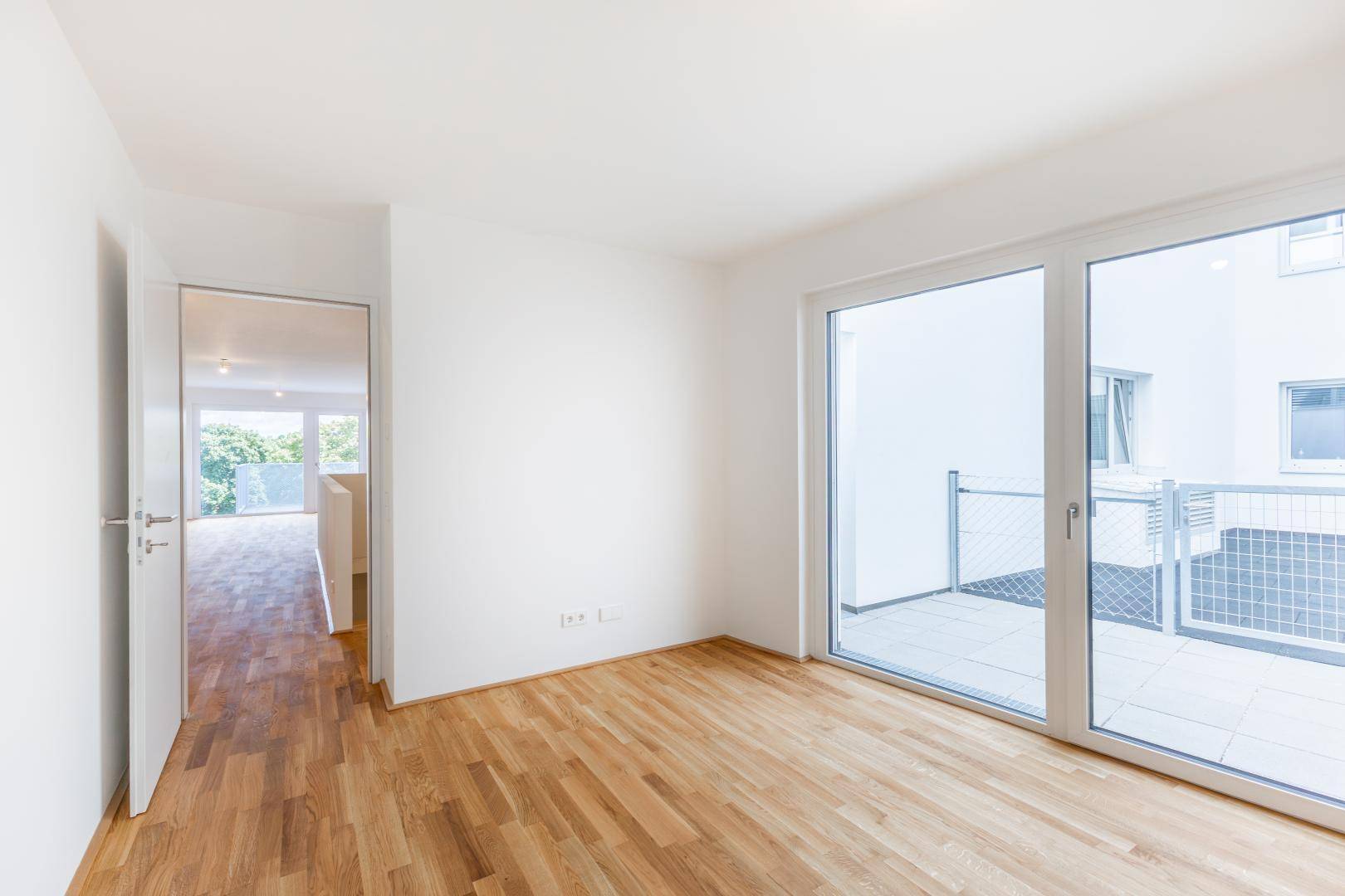 Helles Schlafzimmer mit Holzboden und großem Fenster mit Zugang zum Balkon.