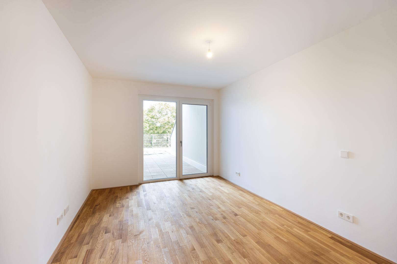 Heller, leerer Raum mit Holzboden und Zugang zu einer Außenterrasse.
