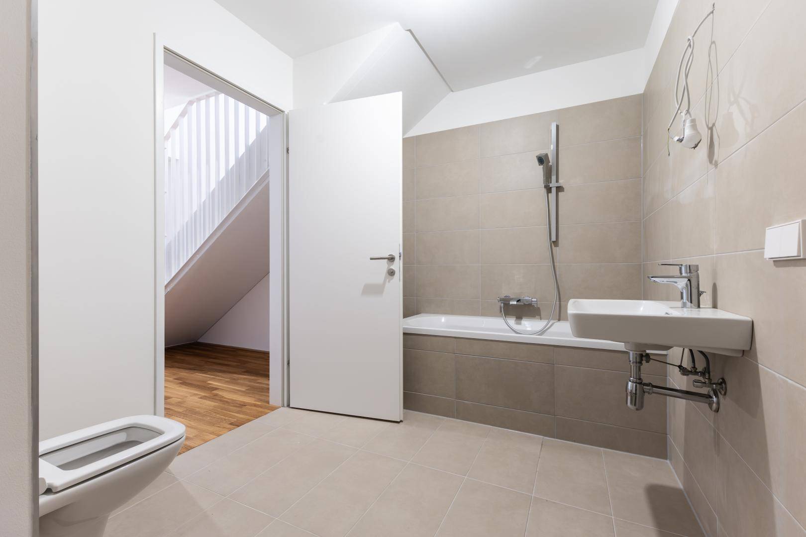 Modernes Badezimmer mit beigefarbenen Fliesen, Badewanne mit Duschfunktion und WC.