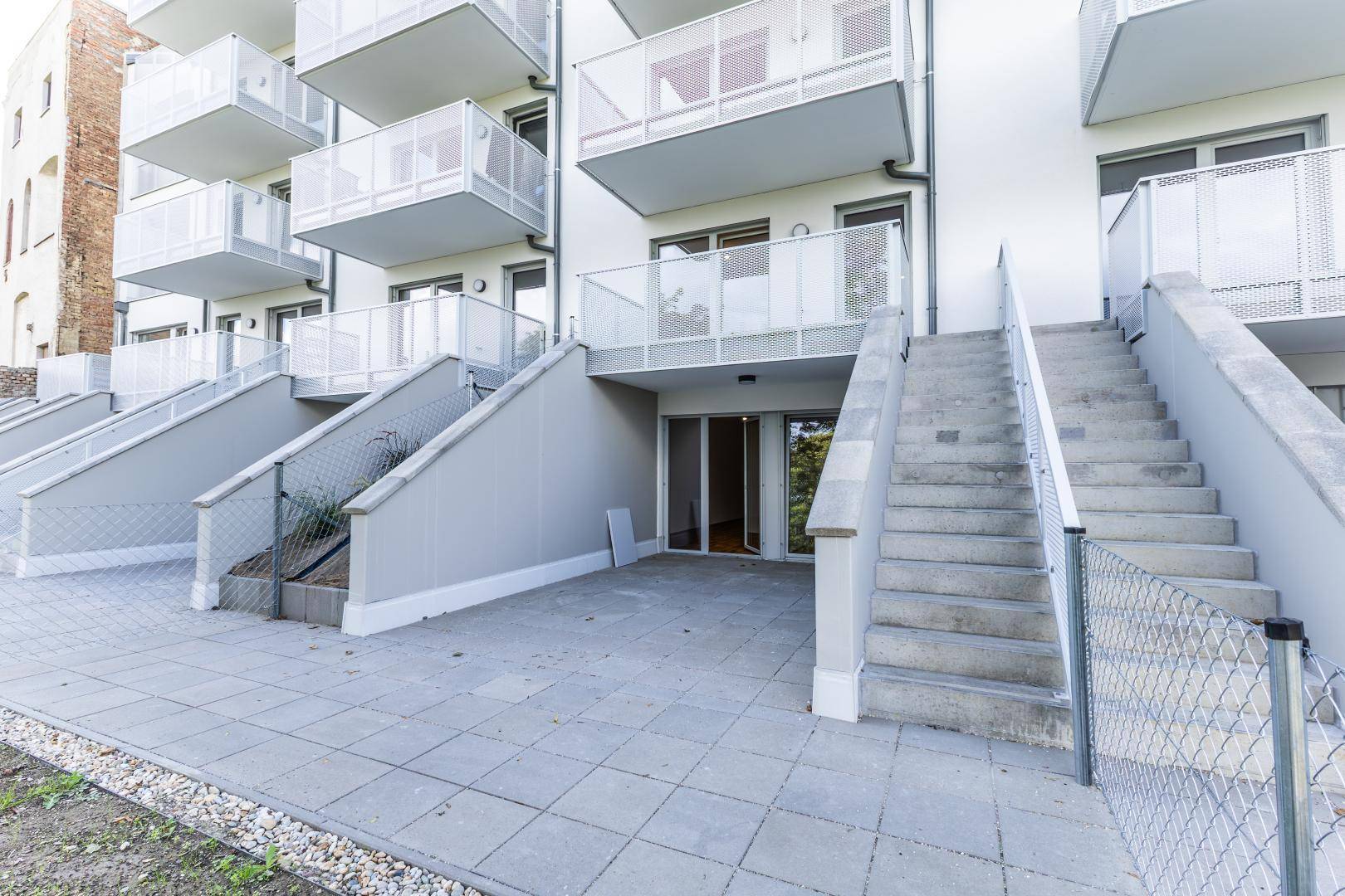 Außenbereich mit gepflasterter Terrasse und Treppen, die zu den oberen Balkonen führen.