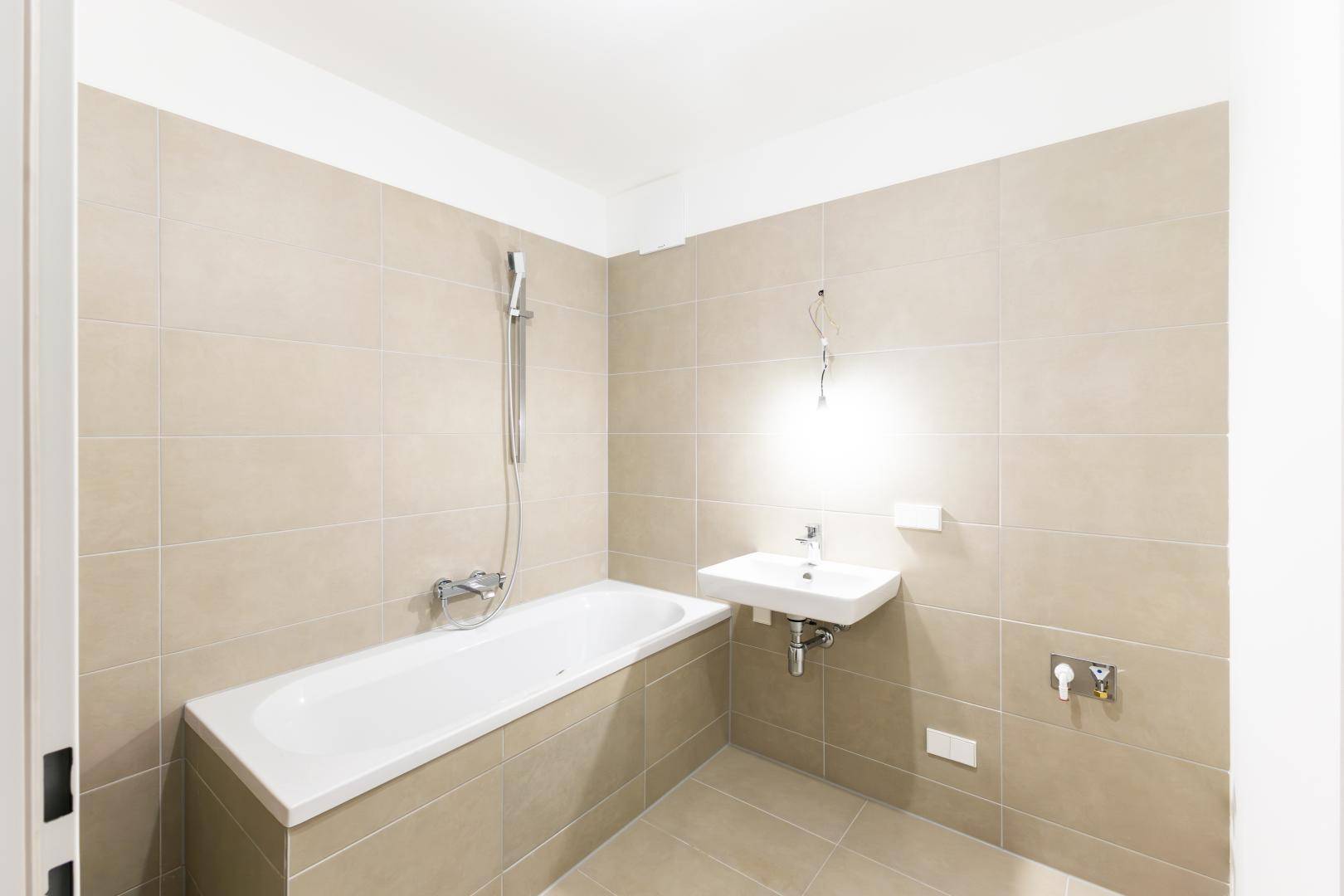 Modernes Badezimmer mit Badewanne, Einzelwaschbecken und beigefarbenen Fliesen.