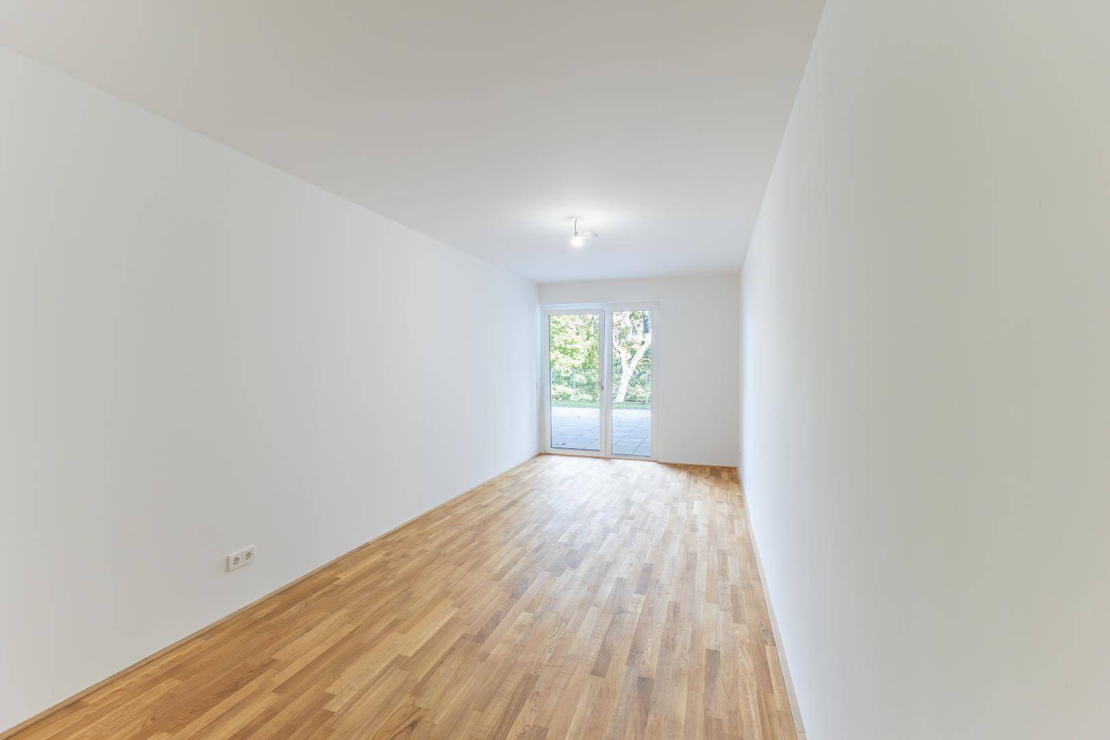 Geräumiger, heller Raum mit Holzboden und großer Glastür, die ins Freie führt.