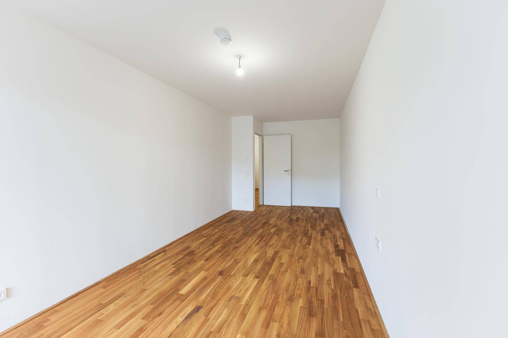 Leeres Zimmer mit hellem Holzboden und weiß gestrichenen Wänden, bereit zum Einzug.