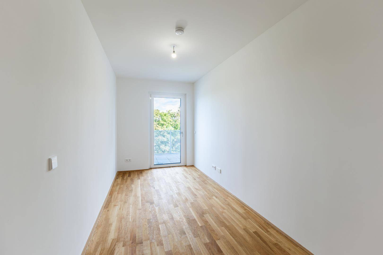 Geräumiges Zimmer mit Holzboden, weiß gestrichenen Wänden und direktem Zugang zum Balkon.
