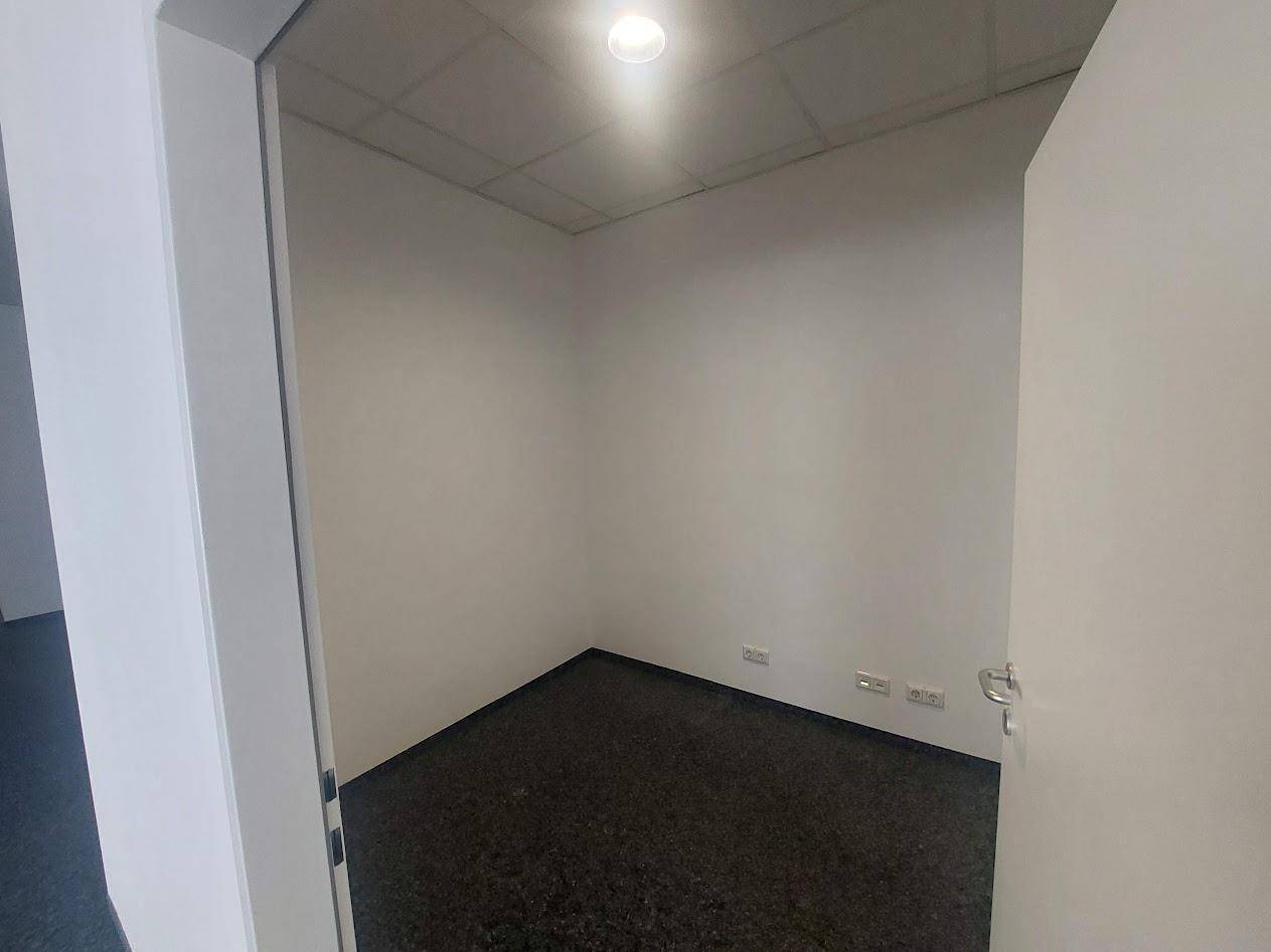 Kleiner, leerer Raum mit dunklem Teppichboden und weißen Wänden, geeignet als Einzelbüro oder Abstellraum.