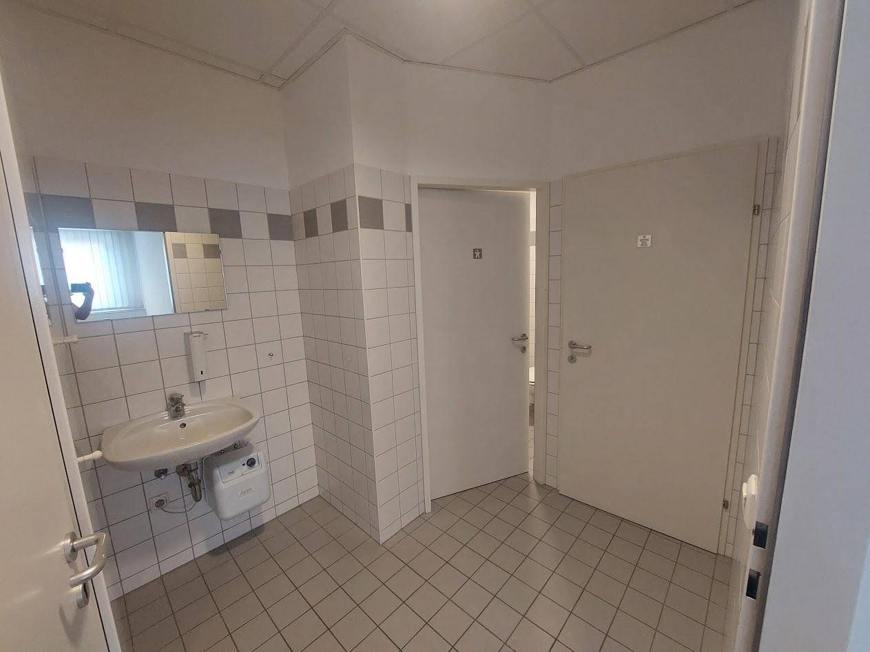 Sanitärbereich mit hellen Fliesen an Wänden und Boden, ausgestattet mit Waschbecken und separaten Toilettenkabinen.