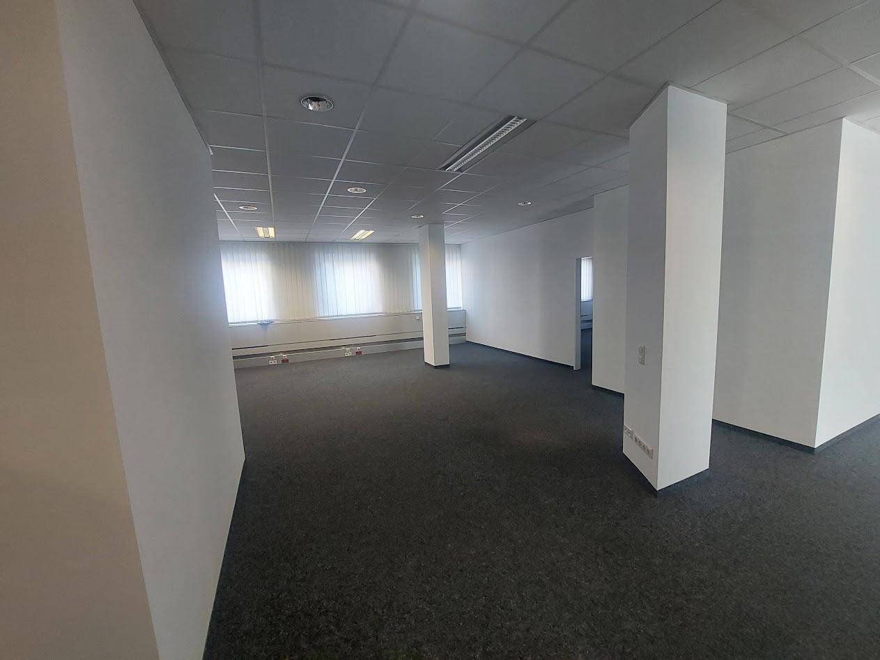 Weitläufiges Büro mit Teppichboden, weißen Wänden und großen Fenstern mit Jalousien, bietet viel Tageslicht.