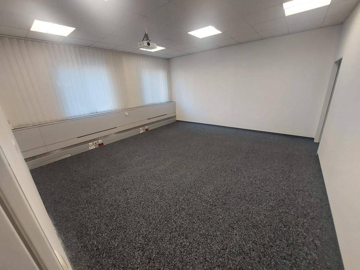 Besprechungsraum oder Büro mit Teppichboden, Fenstern und Deckenprojektor, ideal für Präsentationen.