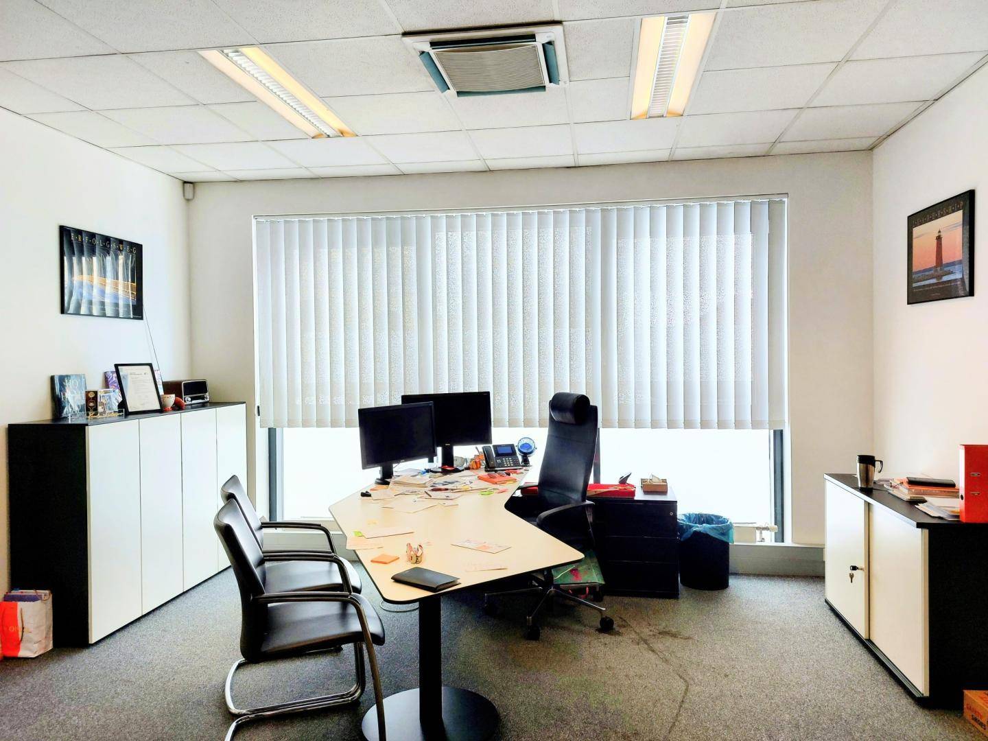 Modernes Büro mit großem Fenster, Jalousien und zwei eingerichteten Arbeitsplätzen mit Computern.